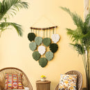 Decorative wall hanging with leaf patterns on a yellow wall, with two wicker chairs and plants in the foreground.