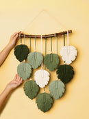 Handmade leaf-shaped wall hanging with green and white leaves on a yellow background