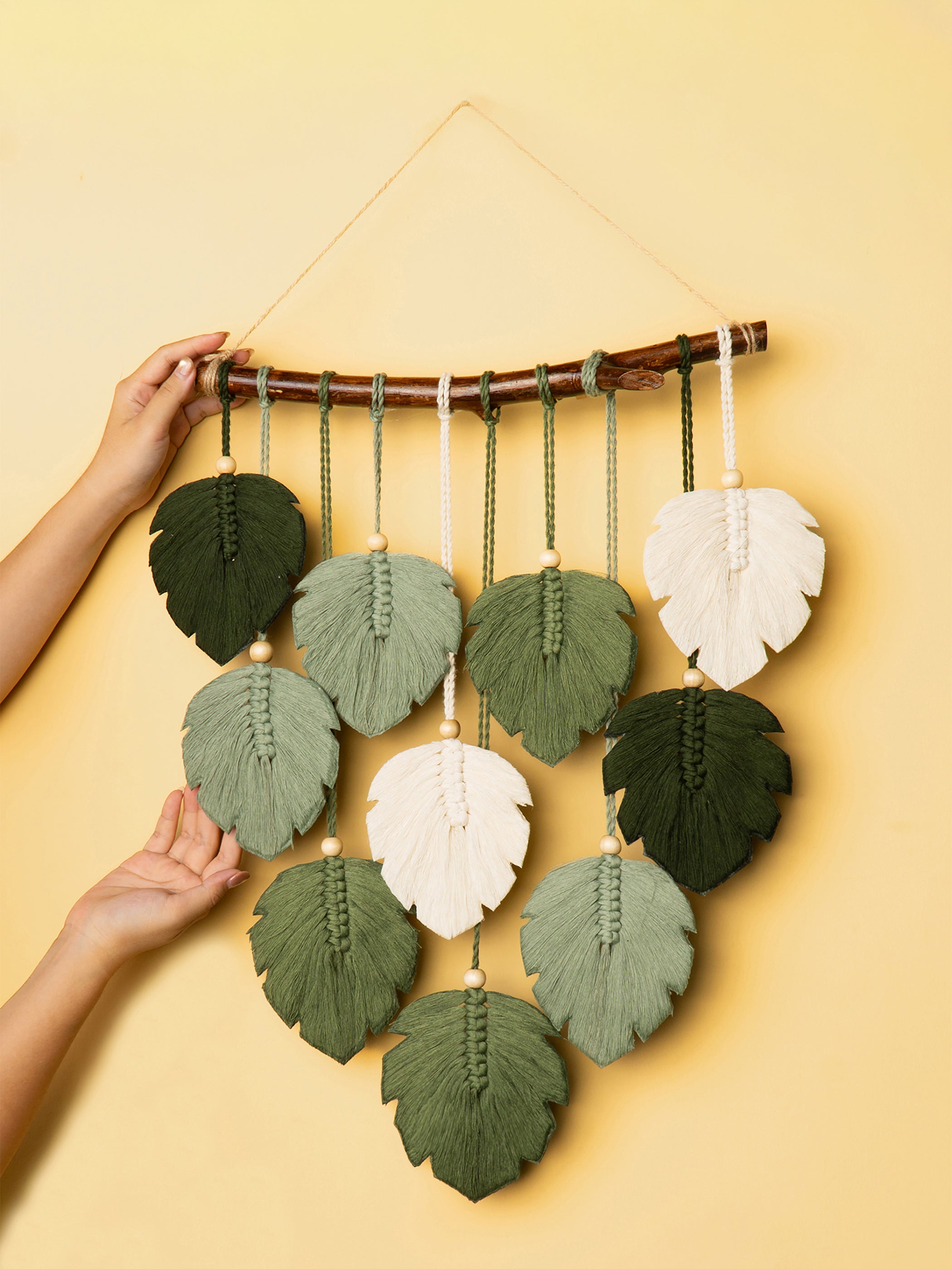 Handmade leaf-shaped wall hanging with green and white leaves on a yellow background
