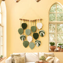 Decorative wall hanging with leaf-shaped elements on a yellow wall with a framed picture.