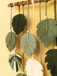 Decorative leaf-shaped ornaments hanging from a wooden rod against a yellow background