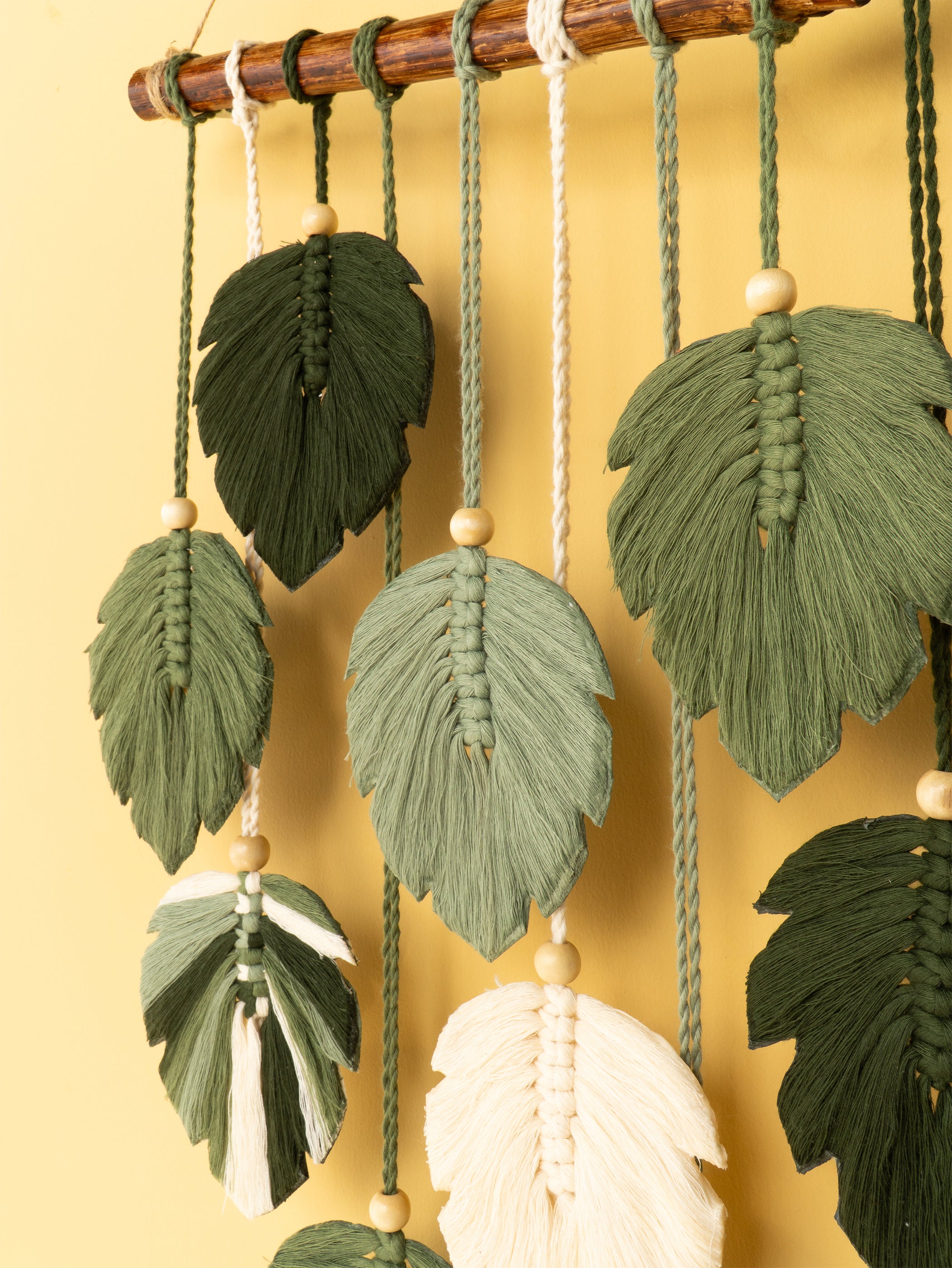 Decorative leaf-shaped ornaments hanging from a wooden rod against a yellow background