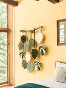 Decorative wall hanging with leaf patterns on a yellow wall next to a window.