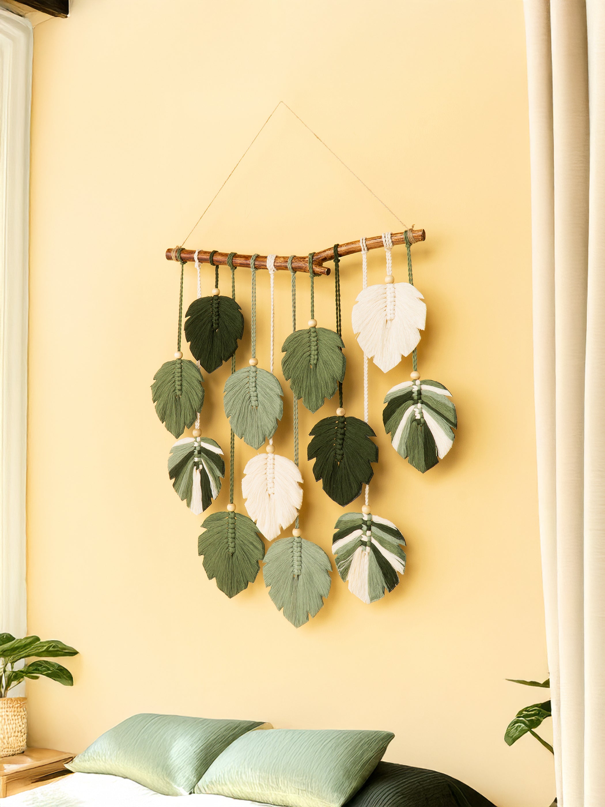 Decorative wall hanging with leaf-shaped ornaments on a yellow wall.