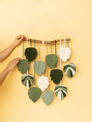 Handmade leaf-shaped decorations hanging from a stick against a yellow background