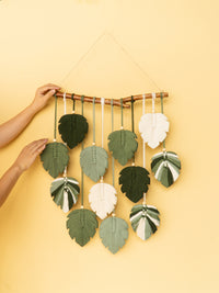 Handmade leaf-shaped decorations hanging from a stick against a yellow background