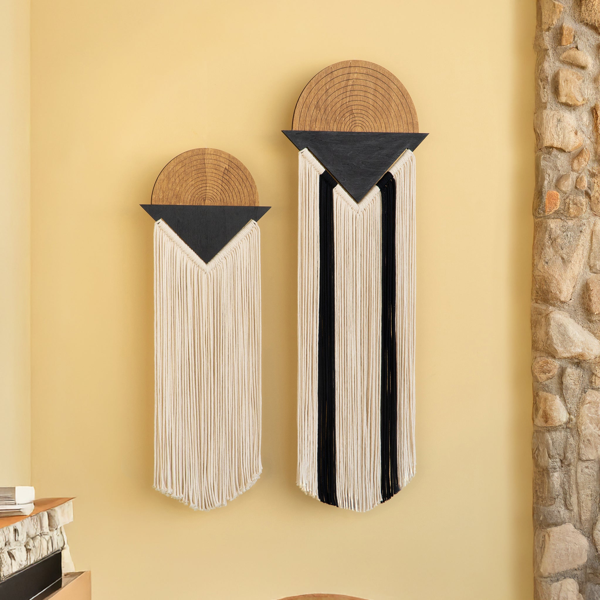 Decorative wall art with circular top sections and striped fringed bottoms on a yellow wall.