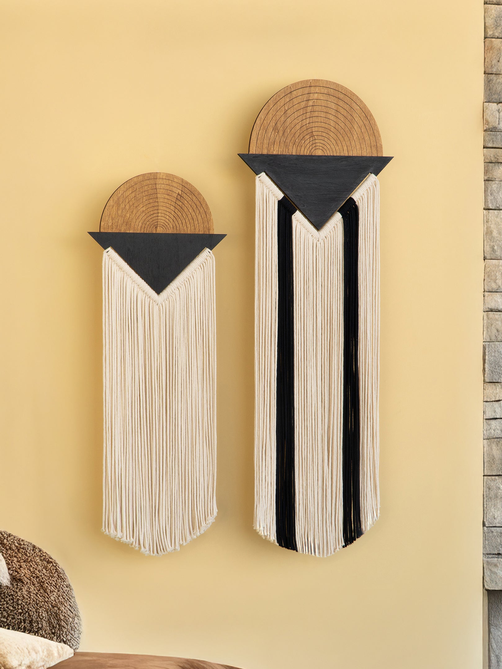 Two wall art pieces with circular top sections and long hanging elements on a beige wall.