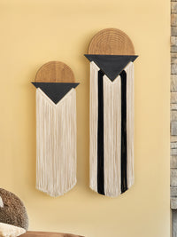 Two wall art pieces with circular top sections and long hanging elements on a beige wall.