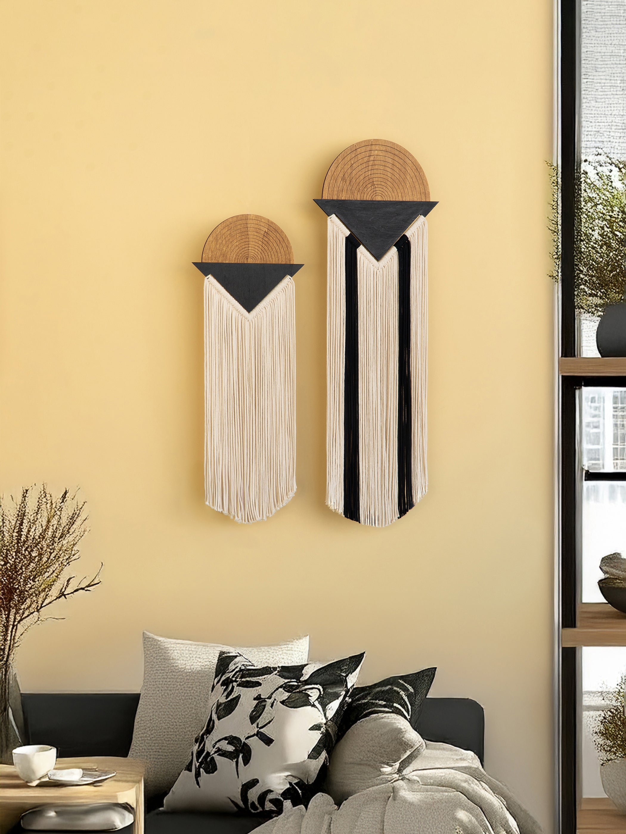 Two wall hangings with wooden tops and fringe on a yellow wall above a sofa.