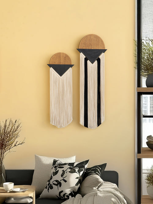 Two wall hangings with wooden tops and fringe on a yellow wall above a sofa.