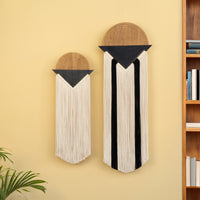 Two wall hangings with geometric designs on a yellow wall next to a bookshelf.