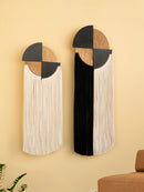 Two geometric wall art pieces with fringes on a beige wall.