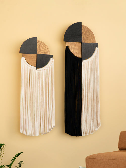 Two geometric wall art pieces with fringes on a beige wall.