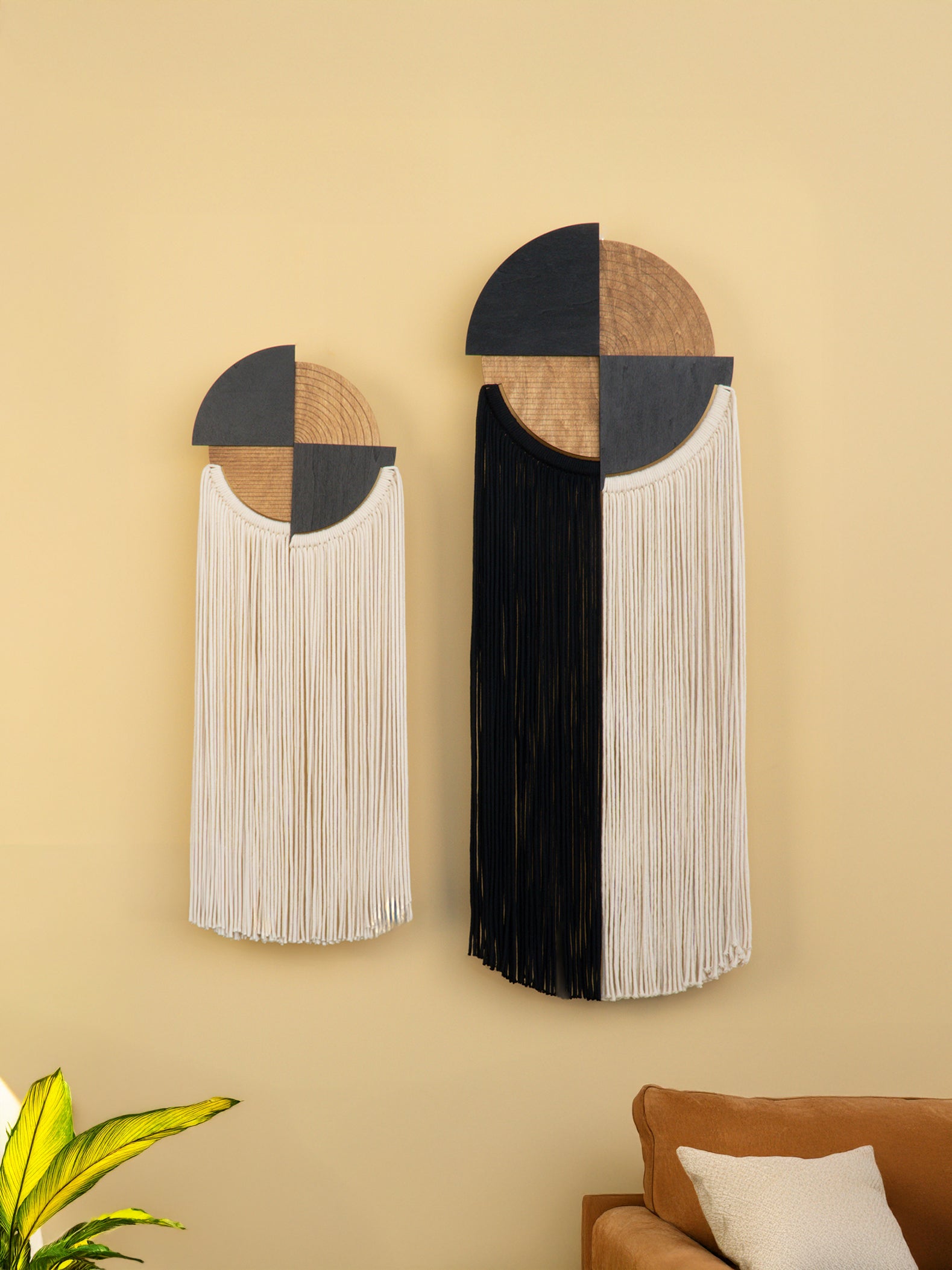 Two geometric wall art pieces with fringes on a beige wall.