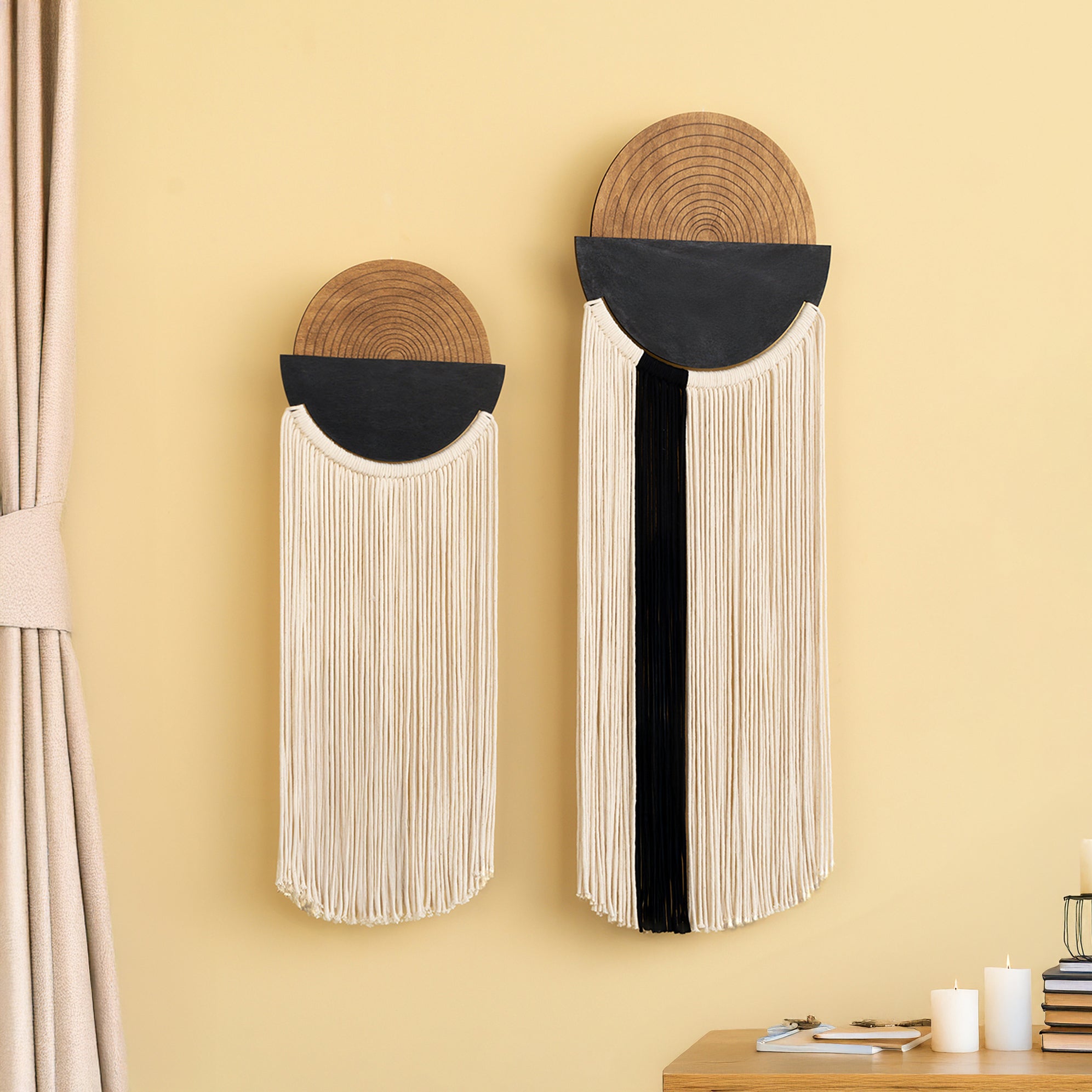 Two wall hangings with circular top and fringed bottom on a yellow wall.