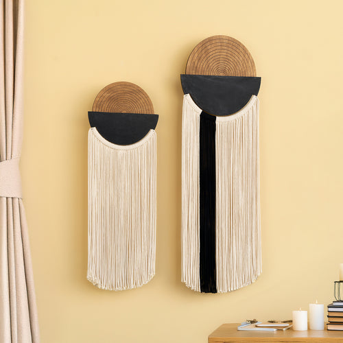 Two wall hangings with circular top and fringed bottom on a yellow wall.