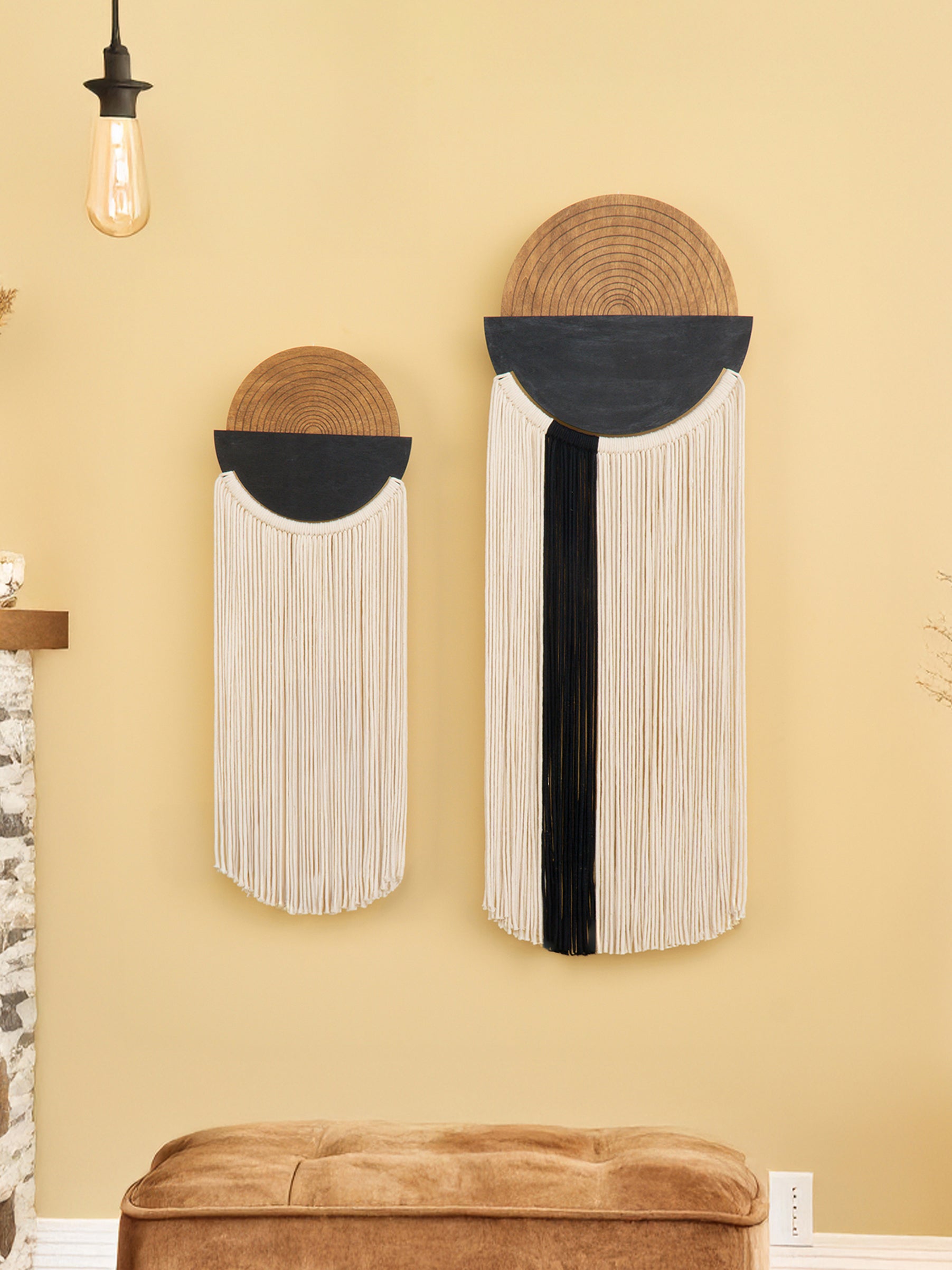 Two wall art pieces with circular designs and fringe on a yellow wall.