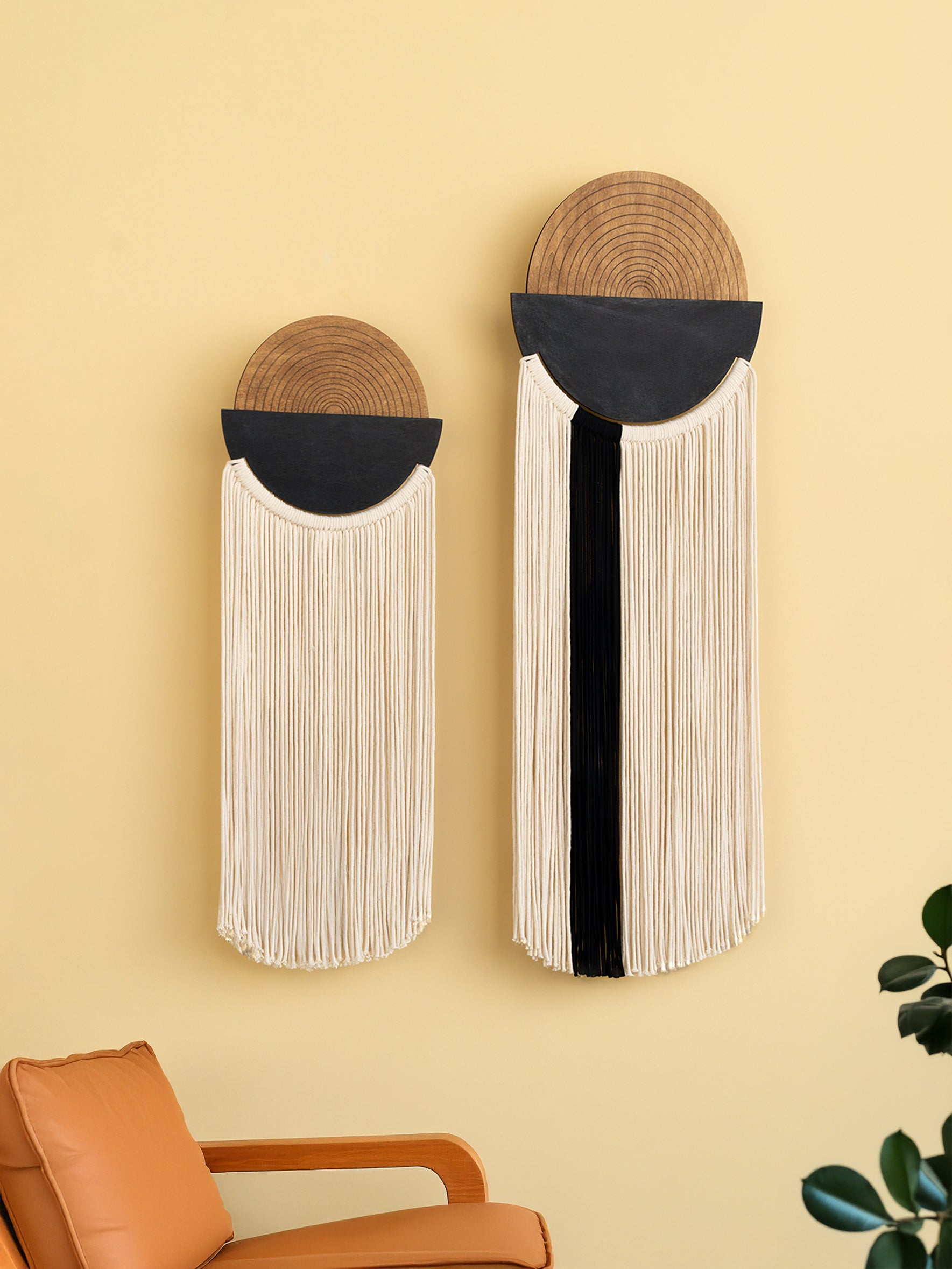 Two wall-mounted decorative items with woven top sections and fringe below on a yellow wall.