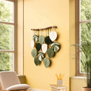 Decorative wall hanging with leaf patterns on a yellow wall in a room with windows and plants.