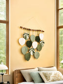 Decorative wall hanging with leaf shapes on a yellow wall above a bed.