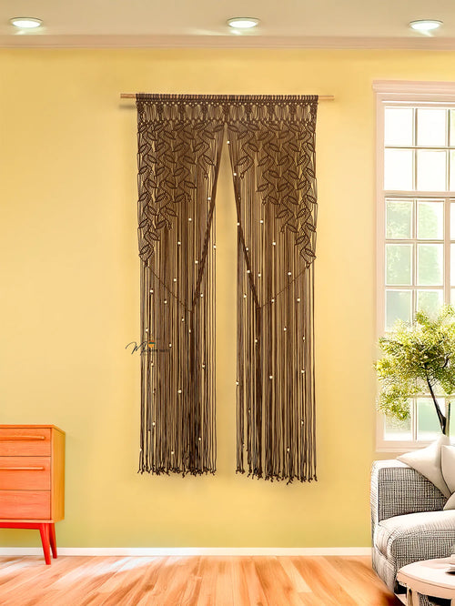 Decorative curtain with tassels hanging on a yellow wall next to a window.