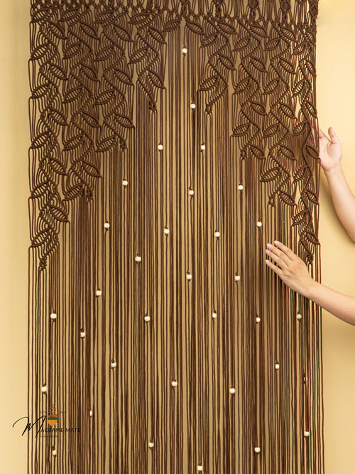 Brown beaded curtain with leaf patterns on a beige wall.