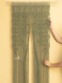 Green embroidered curtain held by a person against a yellow wall