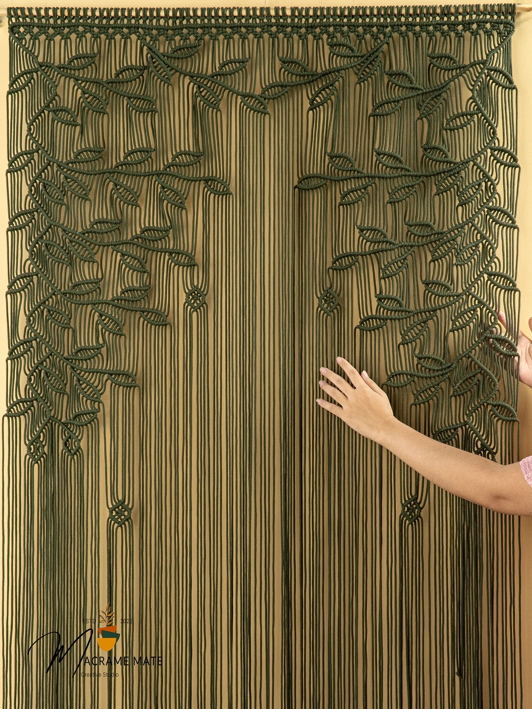 Decorative curtain with leaf pattern held by a hand, brand visible