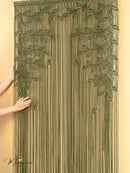 Decorative string curtain with leaf patterns held by a person against a beige background
