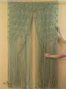 Green macramé curtain being held against a yellow wall