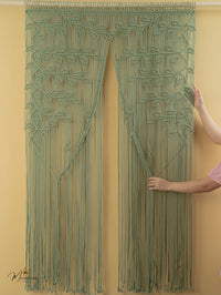 Green macramé curtain being held against a yellow wall