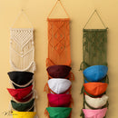 Three macrame hat racks with colorful hats on a beige wall.