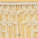 A close-up of a textured fabric or wallpaper featuring a stylized tree design with orange-brown branches and leaves on a warm beige background, accented with small white beads.