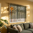 An olive green macrame wall hanging with embroidered leaf patterns and small white bead lights, displayed above a rustic wooden headboard in a bedroom with pink bedding.