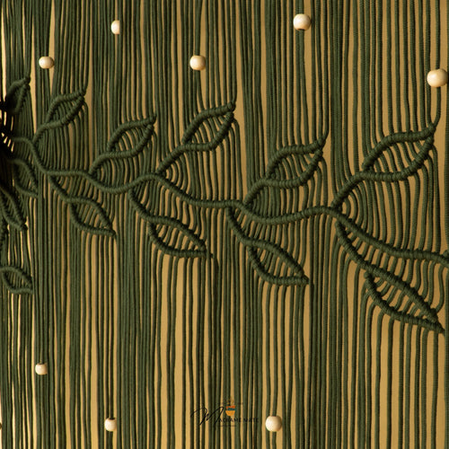 A close-up of a cream-colored macrame wall hanging with intricate woven leaf patterns over a textured vertical background.