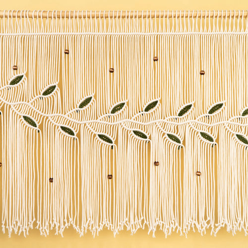 A close-up of a cream-colored fringe curtain or wall hanging with embroidered olive branches and small brown beads, shown against a warm yellow background.