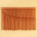 A rust-orange macrame wall hanging with woven branches, leaf patterns, and small white bead accents, suspended against a solid beige background.