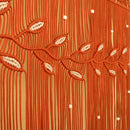 Close-up of a textured orange fringe fabric with woven leaf patterns and small white bead accents.
