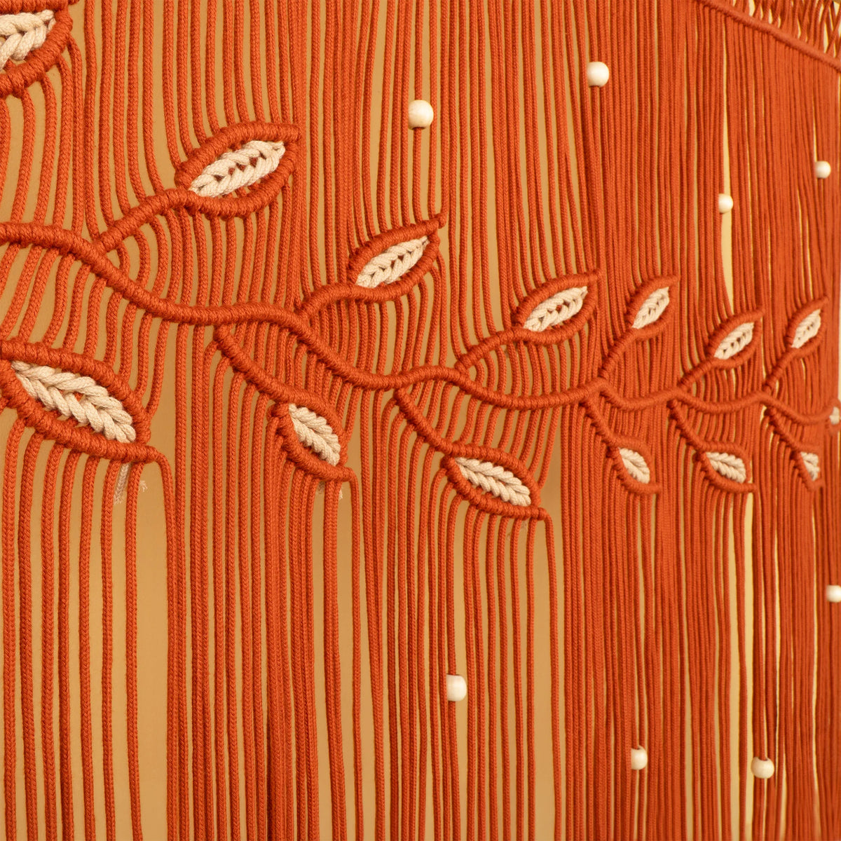 Close-up of a textured orange fringe fabric with woven leaf patterns and small white bead accents.