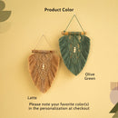 Two woven wall hanging macrame leaf-shaped ornaments on a warm beige background. One is labeled 'Latte' in natural tan and the other 'Olive Green' in muted green, both with wooden dowels, string hangers, and small pearl-like beads at the center.