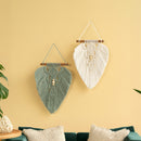 Two macrame wall hangings on a yellow wall with a teal sofa and plant.