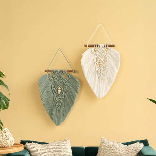 Two macrame wall hangings on a yellow wall with a teal sofa and plant.