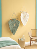 Decorative wall hangings on a yellow wall with a wicker chair and small table.