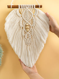 Macrame wall hanging held by a hand against a yellow background