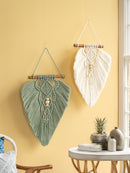 Two macrame wall hangings on a yellow wall with a small table and chair in the foreground.