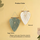Two macrame wall hangings displayed against a warm beige background, labeled 'Product Color' with options 'Sage Green' and 'Natural'. The left hanging is sage green with a central wooden bead, and the right hanging is natural cream with a central wooden bead.