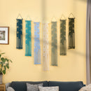 Six macrame wall hangings with leaf patterns in various colors (dark blue, teal, light blue, cream, sage green, and black) are displayed on a yellow wall above a dark blue sofa in a living room setting.