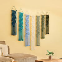 Set of six macrame wall hangings in various colors on a yellow wall.