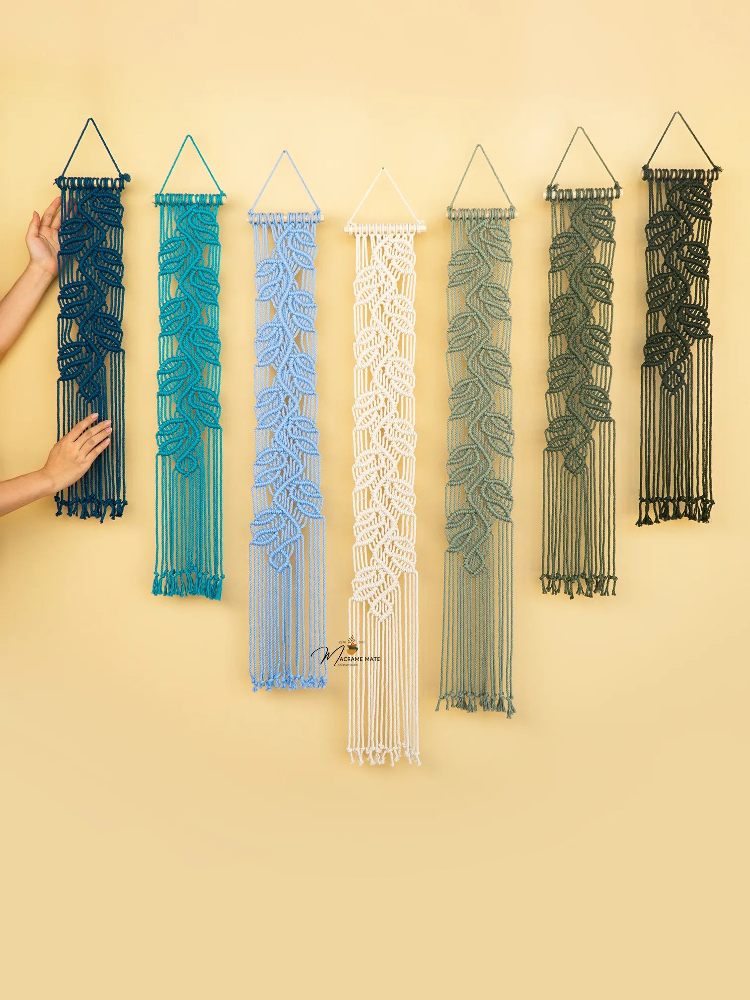 Set of six macrame wall hangings in various colors on a yellow background